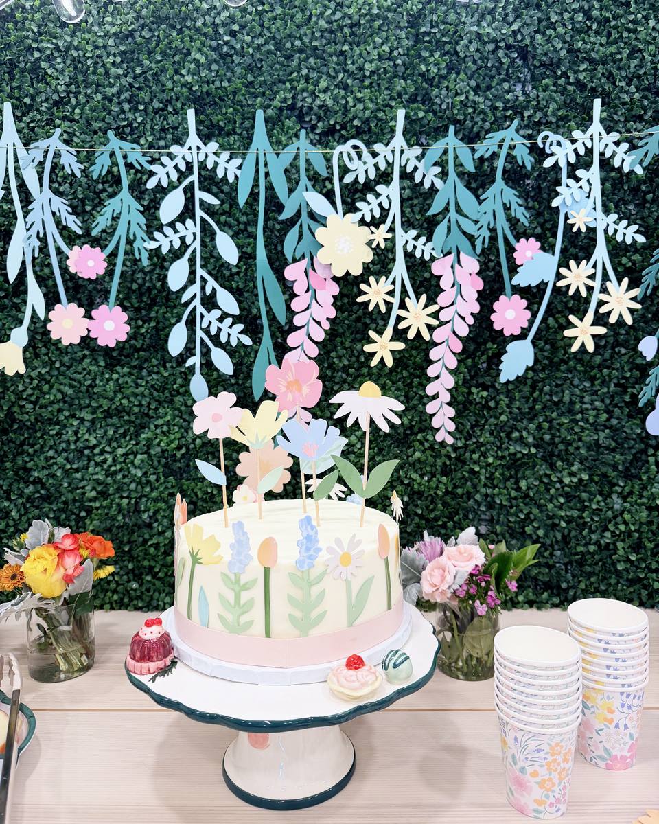 Flower cake on a stand in front of a paper flower garland
