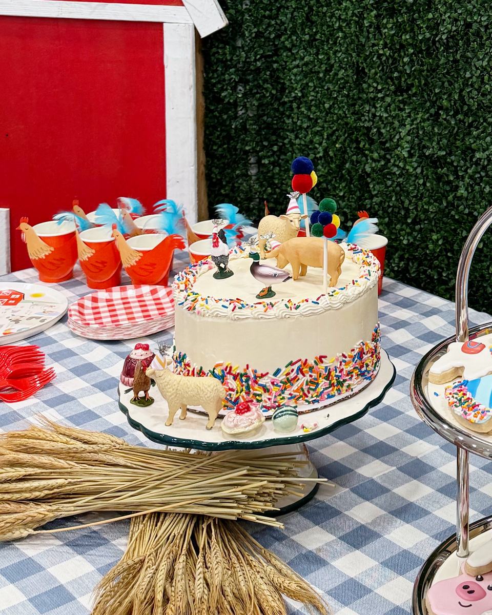 Farm-themed birthday cake with animal toppers on a checked tablecloth